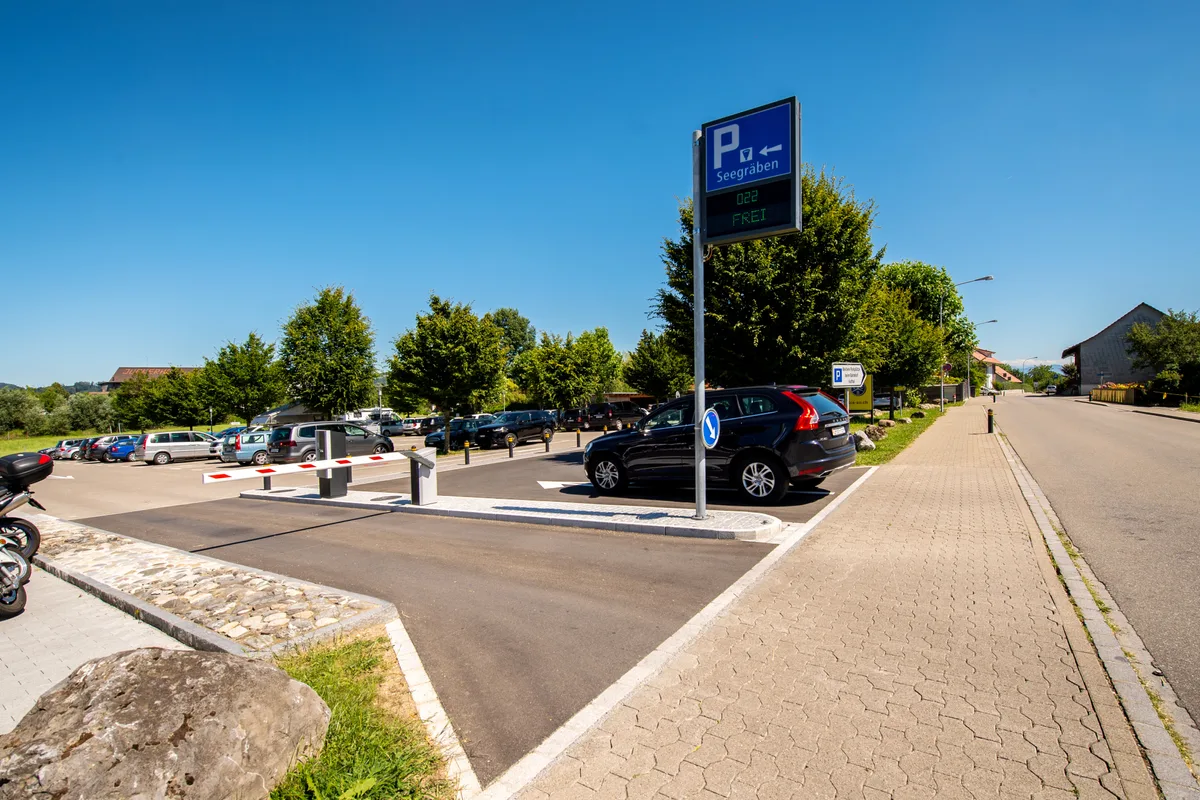 Einfahrt zu einem Parkplatz mit Schranke und Parkleittafel. 